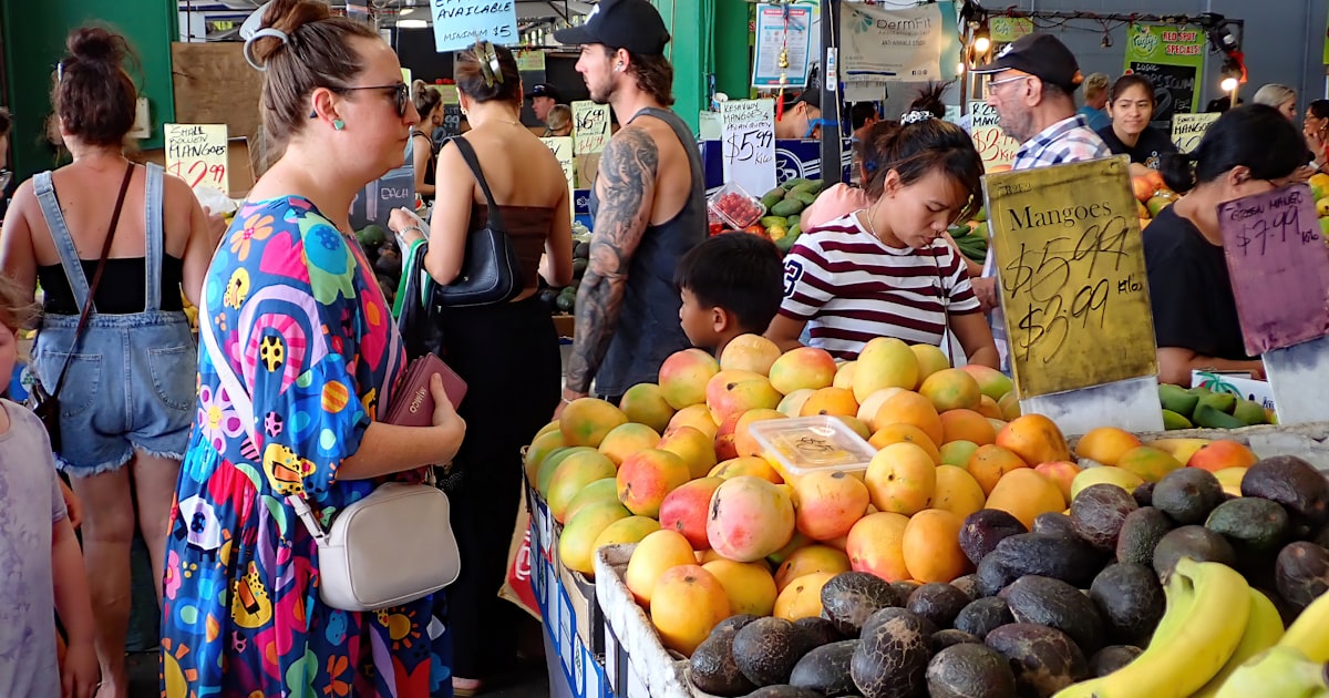a group of people standing around a fruit stand