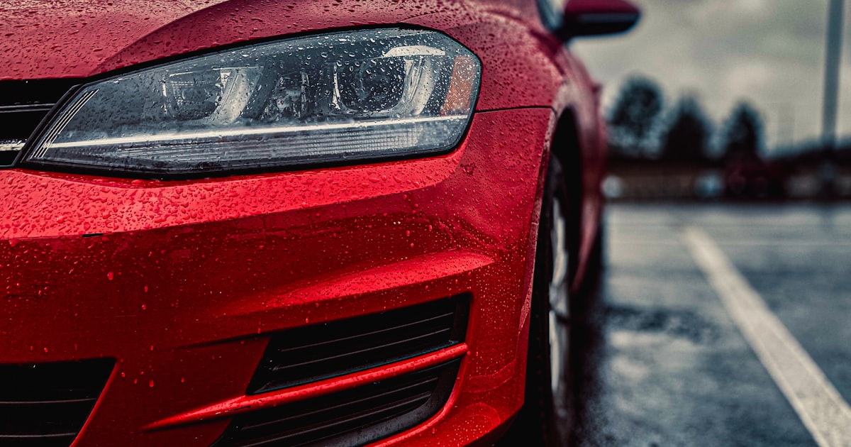 a red car parked on the side of the road in the rain