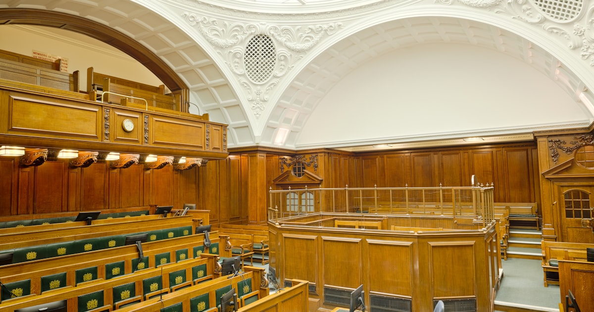 Empty ornate courtroom interior with wooden paneling and green seats.
