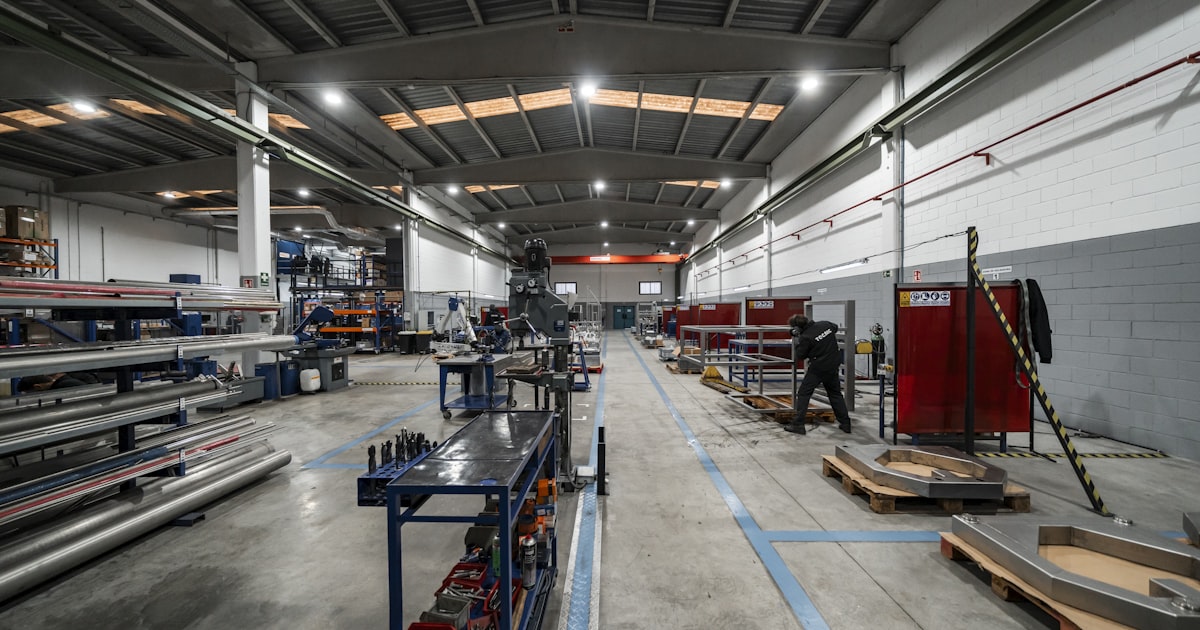 Inside a large factory, equipment and workers are present.