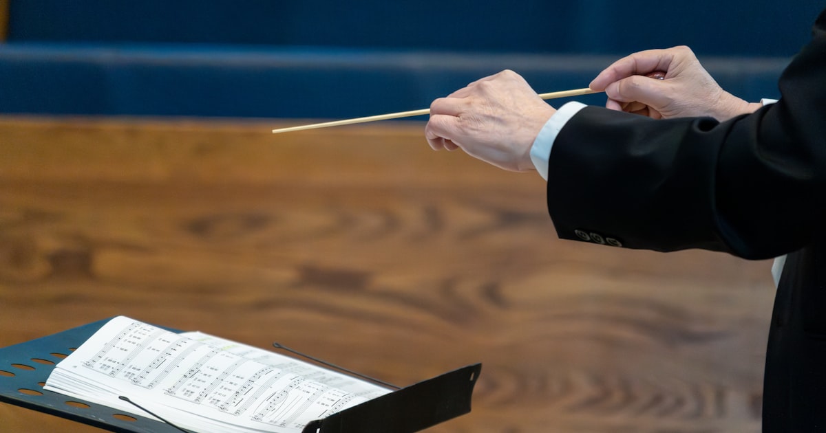 Conductor leading orchestra with baton over sheet music