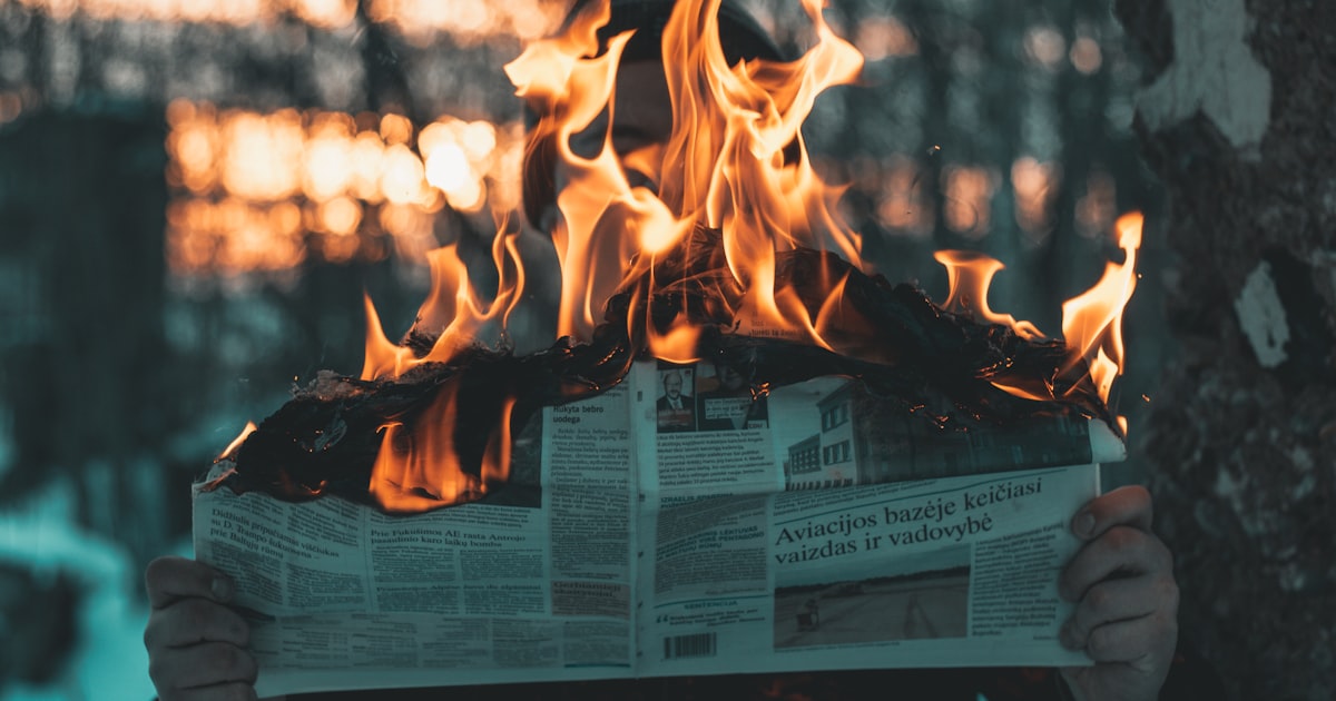 A person holding a newspaper in front of a fire