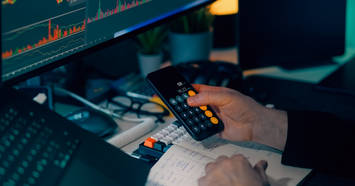 Person using calculator at desk with computer charts.