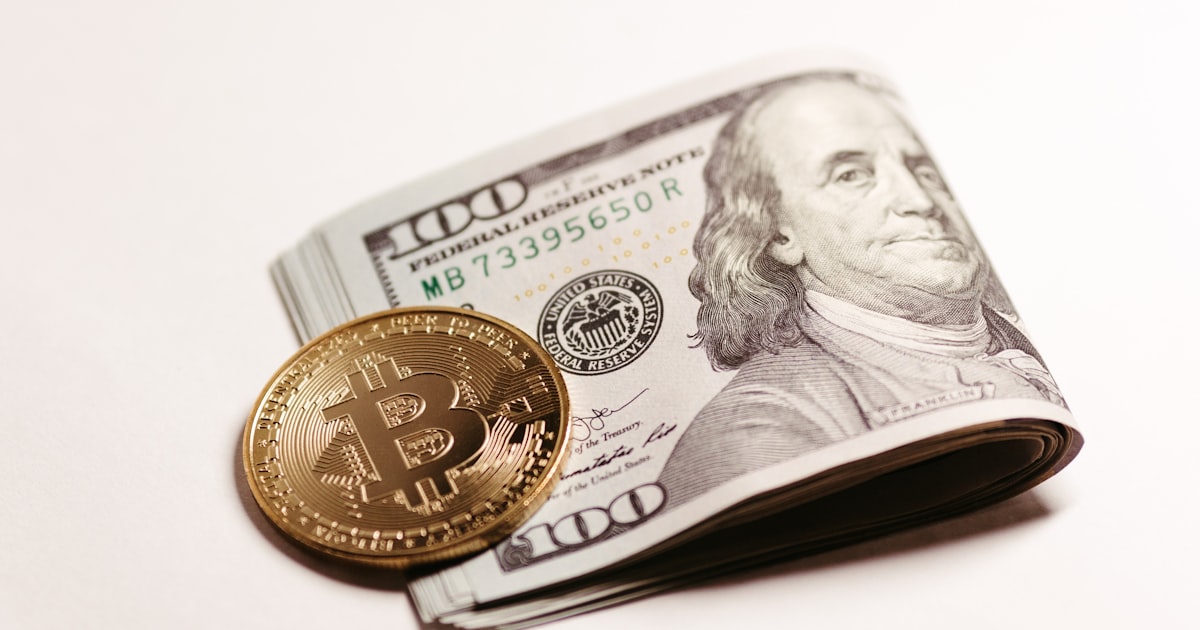 a stack of one hundred dollar bills and a bitcoin