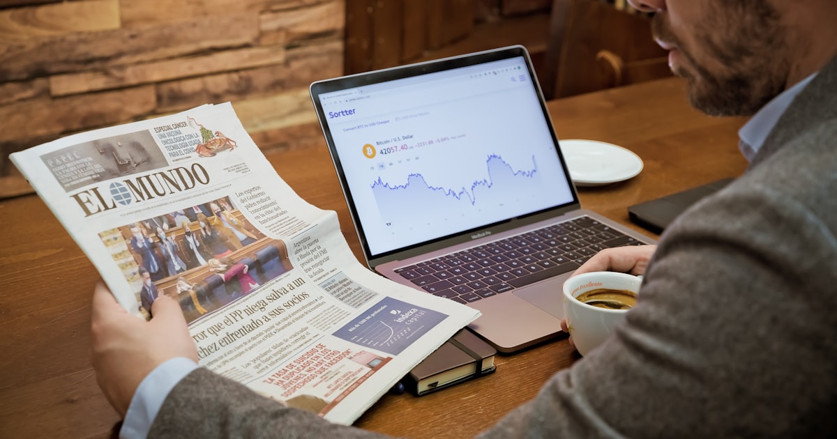 a man reading a newspaper while using a laptop