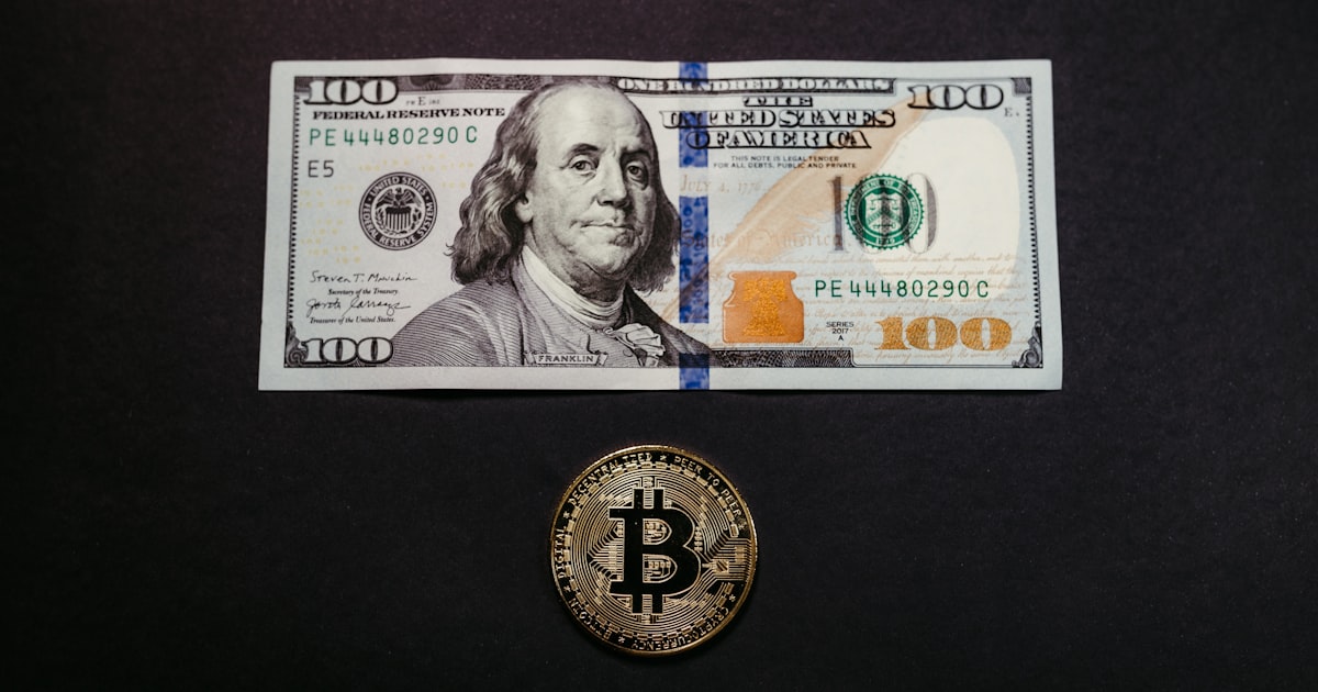 a $ 100 bill and a bitcoin on a table