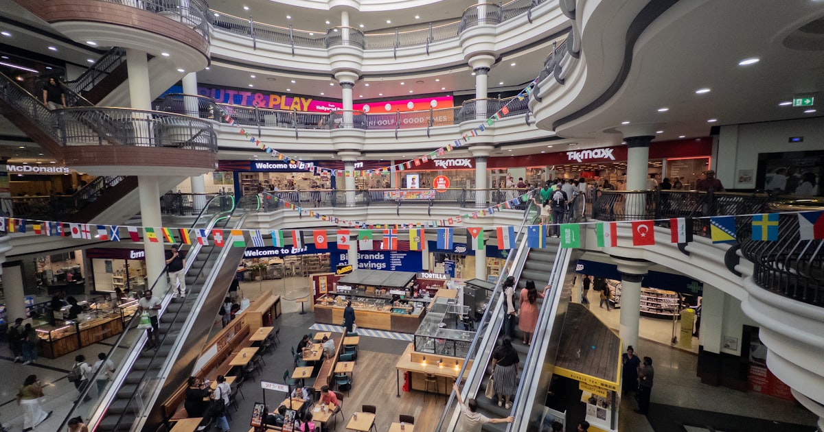 A bustling multi-story shopping mall interior with escalators and shops.