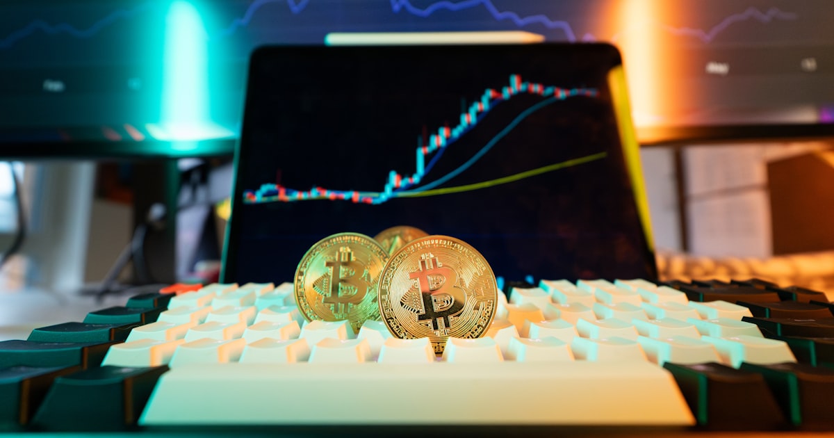 Bitcoin coins rest on a keyboard with stock charts.