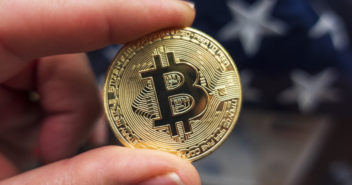 a hand holding a bit coin in front of an american flag