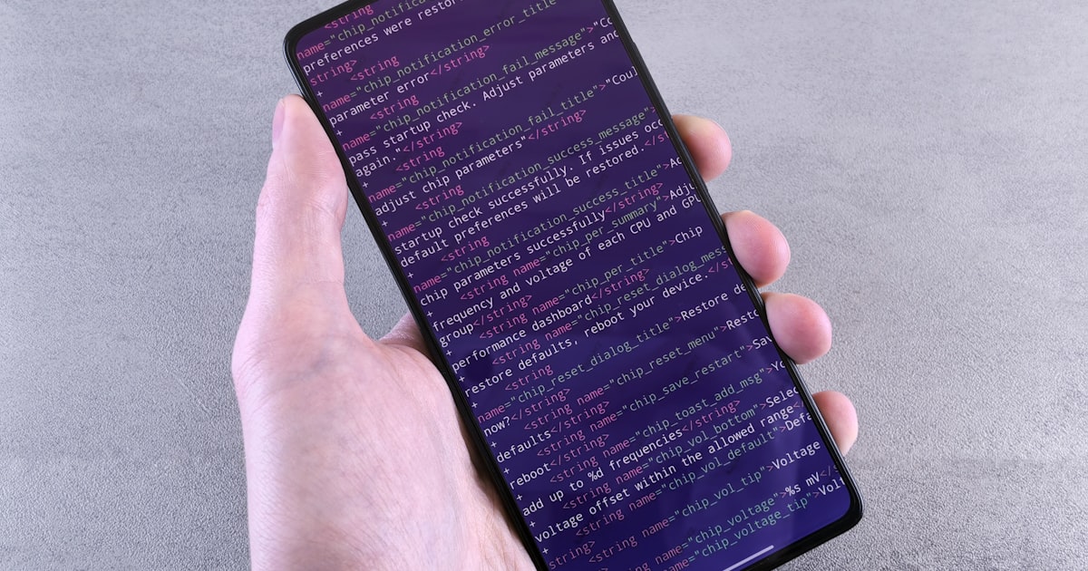 Hand holding smartphone displaying lines of code