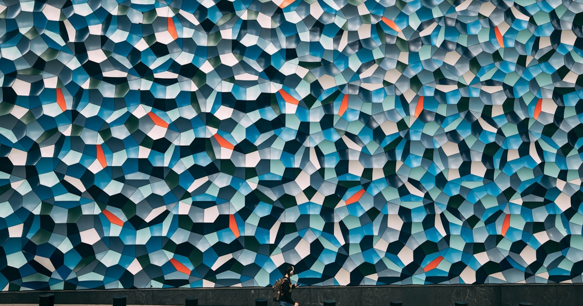 Person walks past a large abstract blue patterned wall.