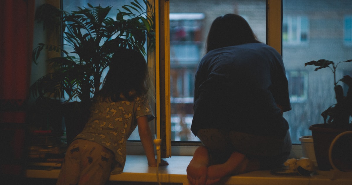 Two people looking out a window at night.