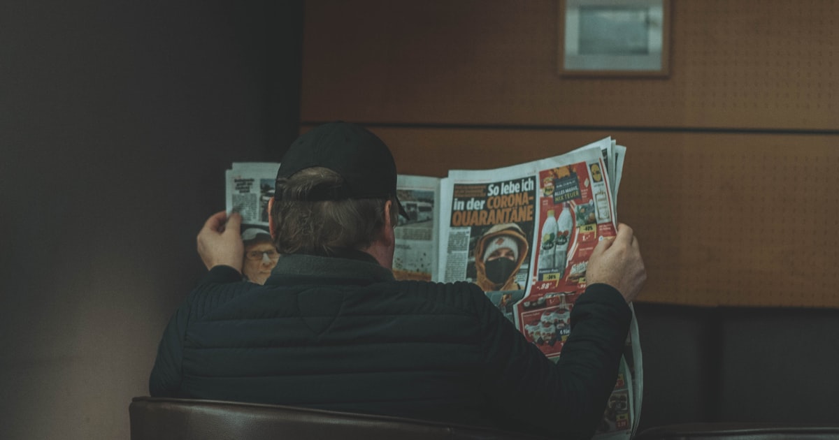 man in black long sleeve shirt reading newspaper