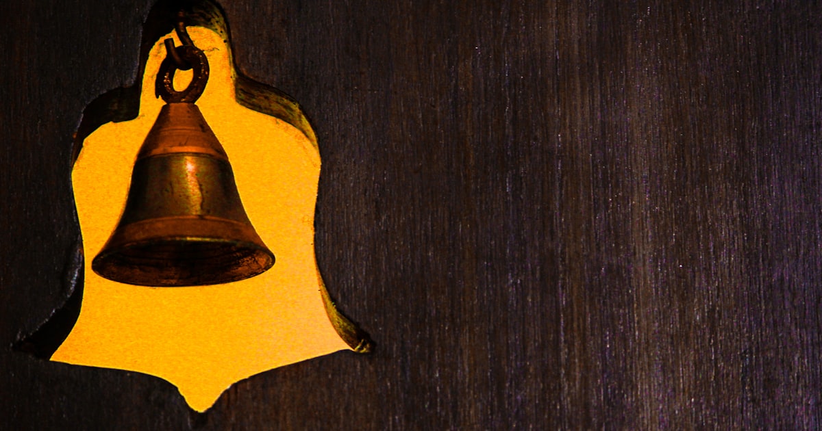 A brass bell hanging on a wooden surface.