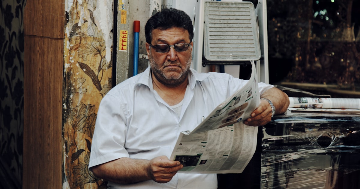 man in white polo shirt reading newspaper