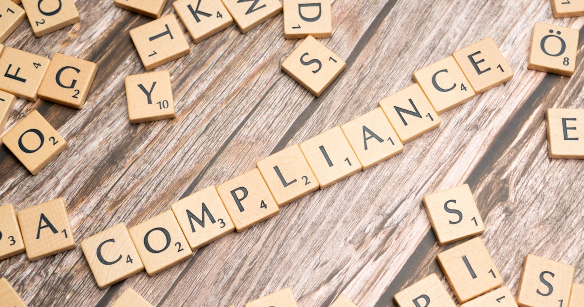 The word compliance spelled out with wooden letter tiles on a rustic table