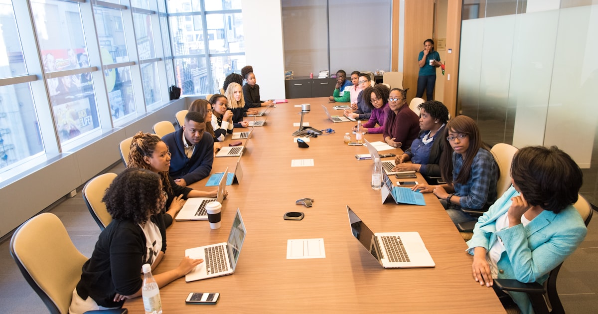people sitting beside rectangular brown table with laptops