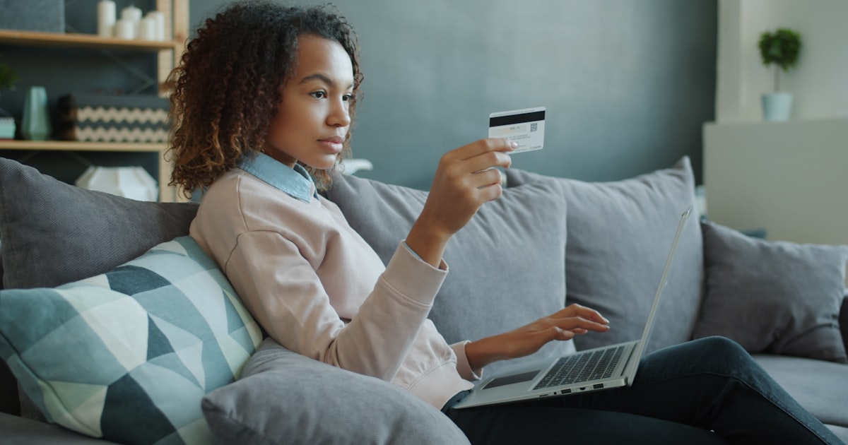 Woman using laptop and credit card on sofa