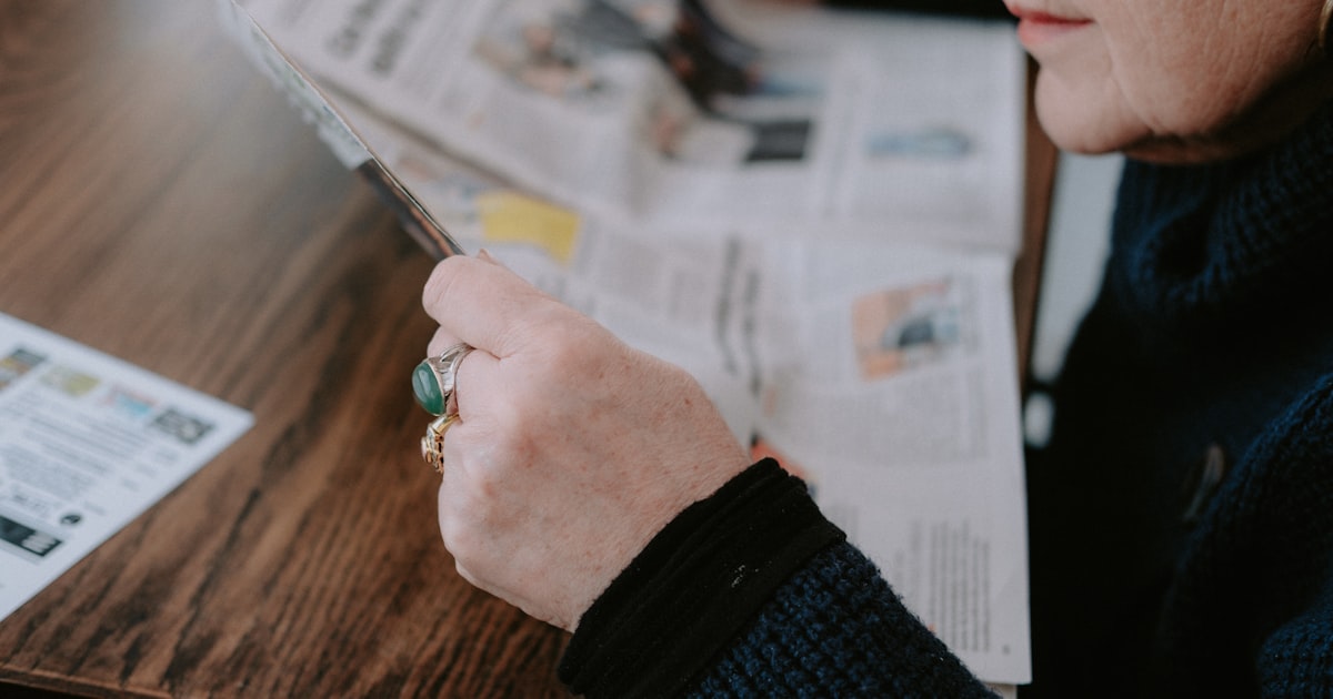 a woman sitting at a table reading a newspaper