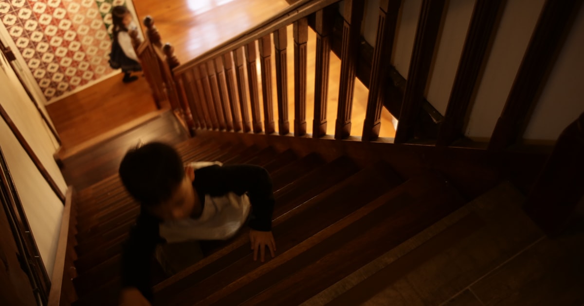 A boy crawls up wooden stairs while a girl watches.