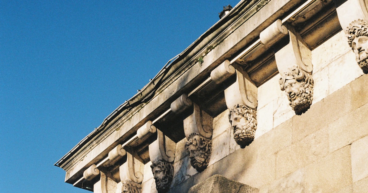 beige stone building with carved head ornate under clear blue sky