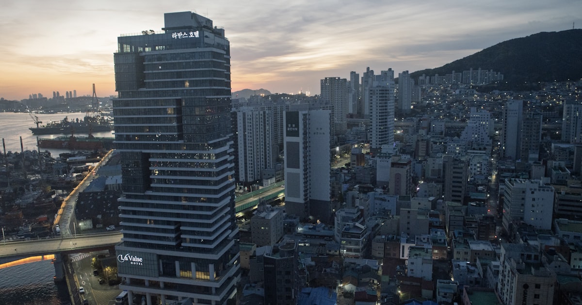 Modern skyscraper in a dense urban cityscape at dusk.