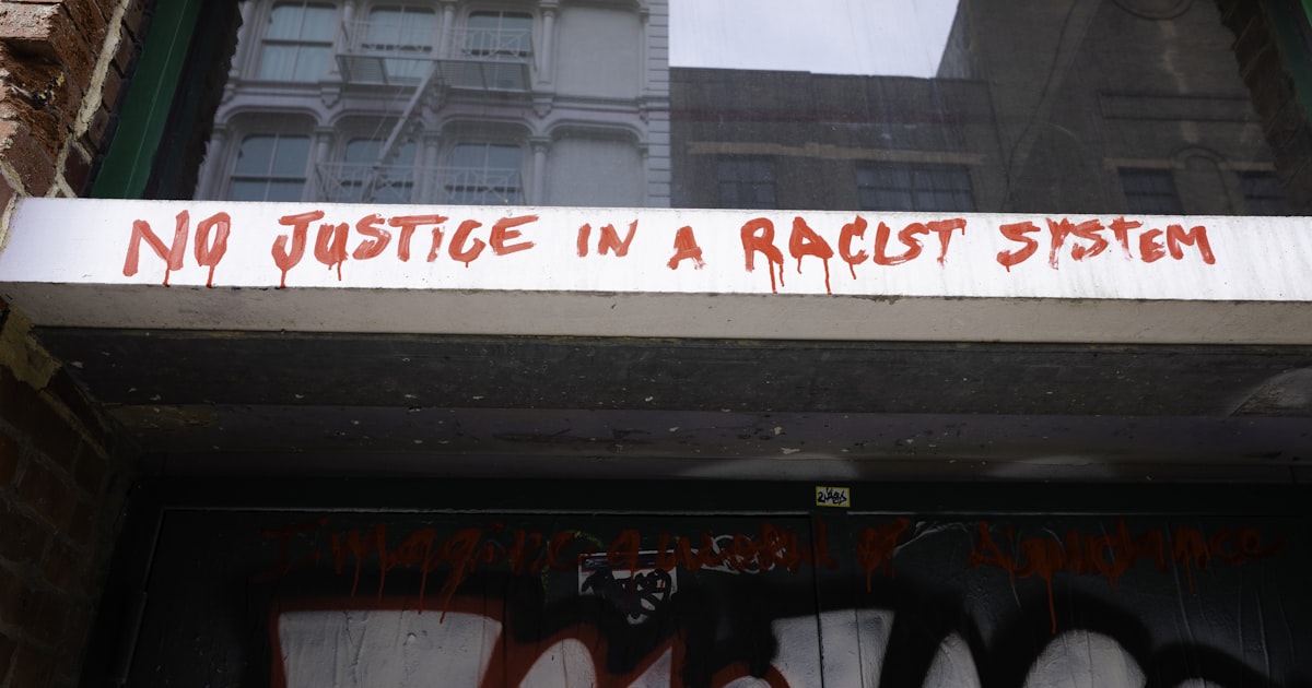 Graffiti reads "no justice in a racist system" on building