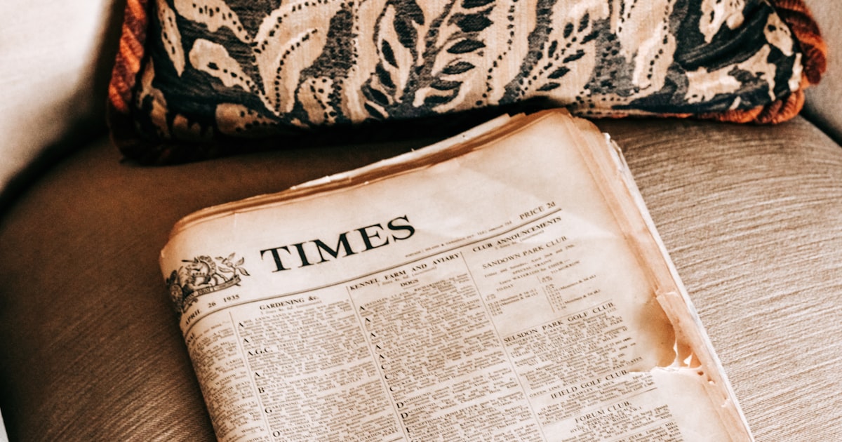 an old newspaper sitting on a couch next to a pillow