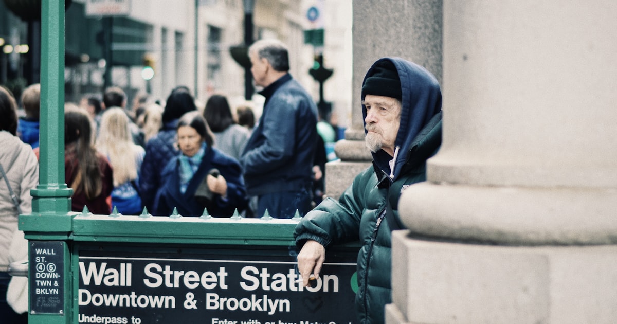 one unknown man standing beside wall street staton downtown and Brooklyn signboard