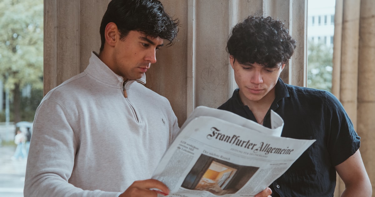 Two men looking at a newspaper while standing next to each other