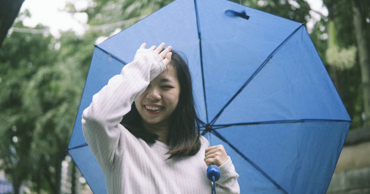 woman in white long sleeve shirt holding blue umbrella