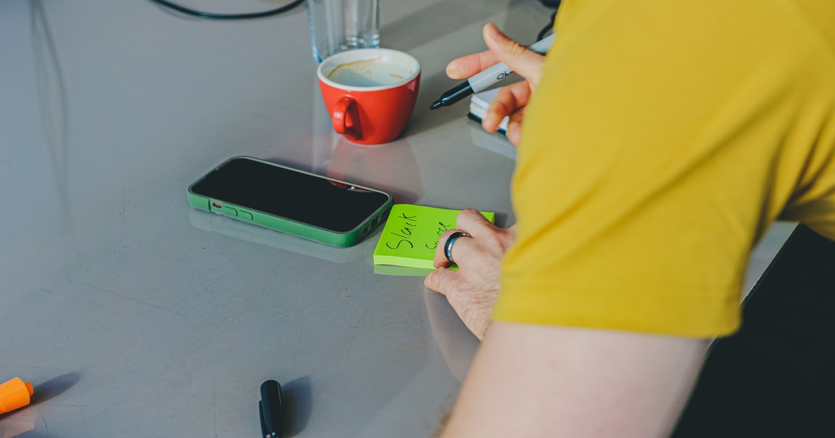 Person in yellow shirt at desk with coffee and supplies.