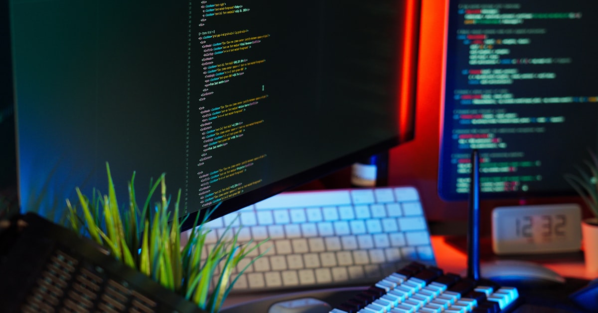 Screens display coding text, representing programming work.