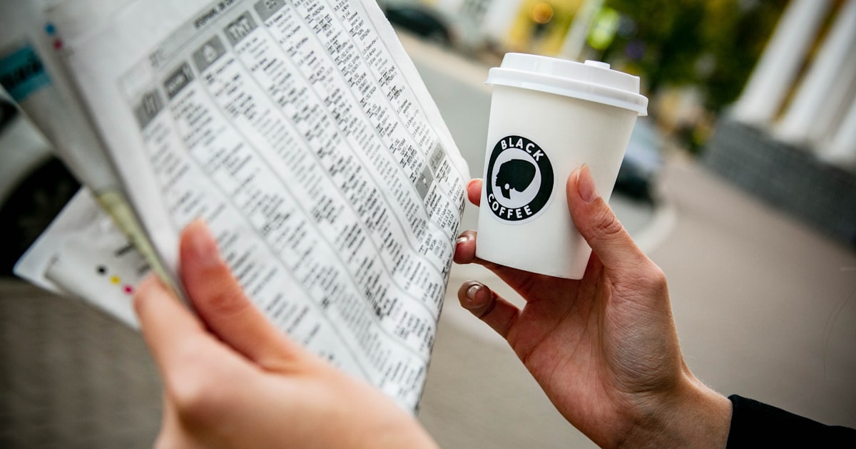 a person holding a cup of coffee and a newspaper