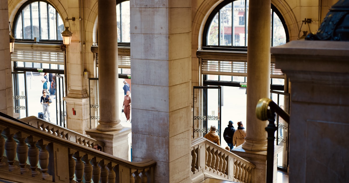 People walking up grand marble staircase with arched windows.