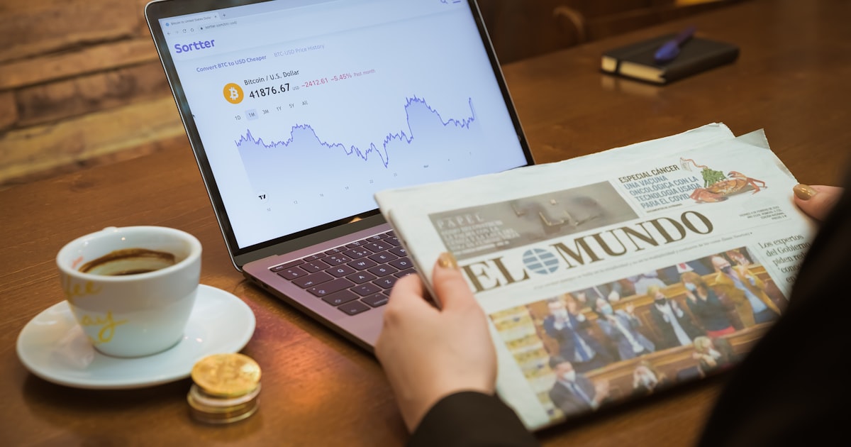 a person reading a newspaper next to a laptop