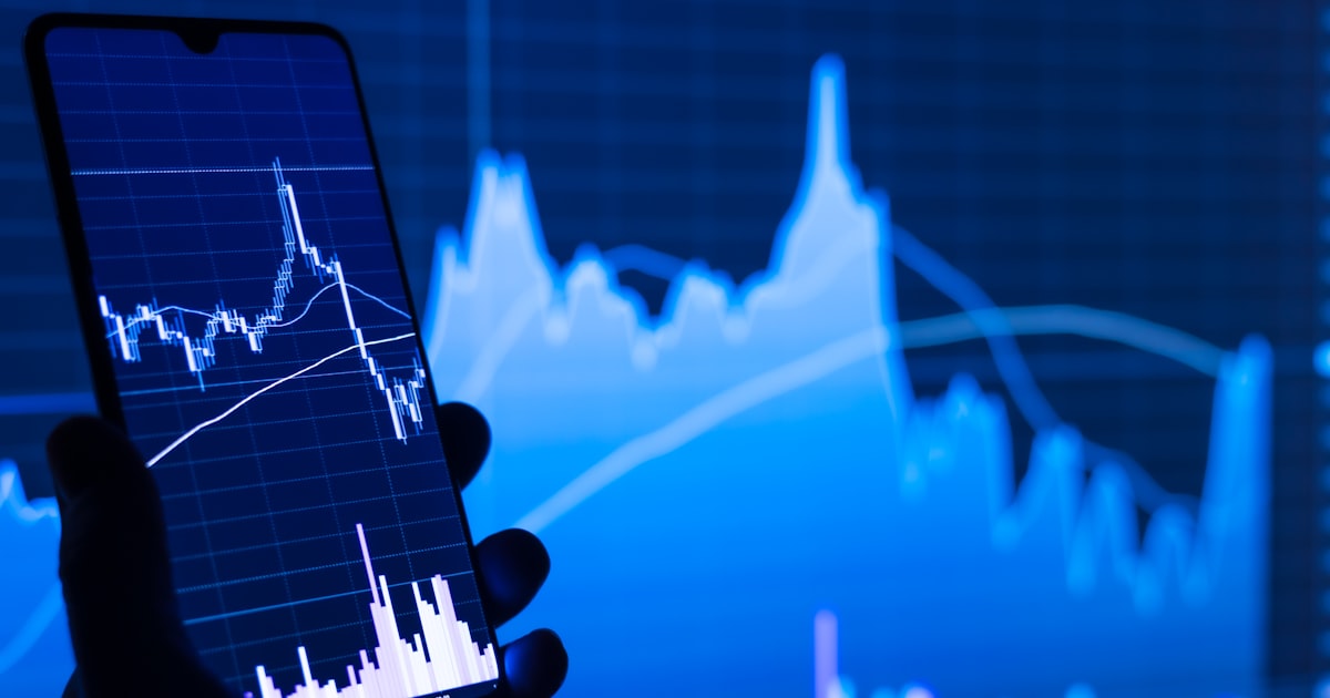 a person holding a cell phone in front of a stock chart