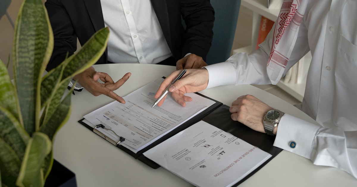 two men sitting at a table with papers and a pen