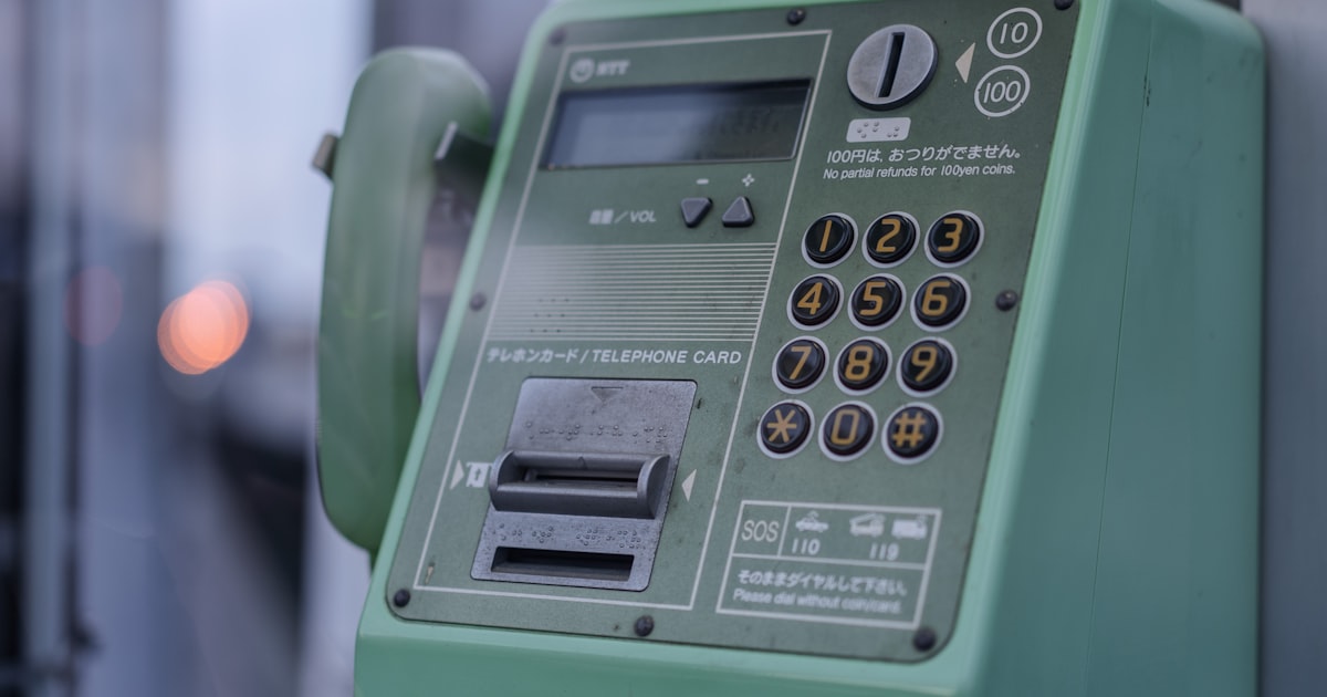 A green public phone booth stands outdoors.
