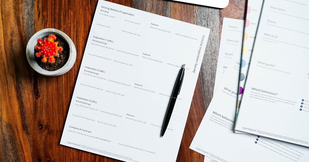 a wooden table topped with papers and a pen