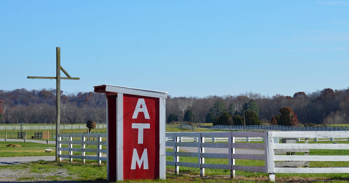 a red and white atm sign next to a white fence