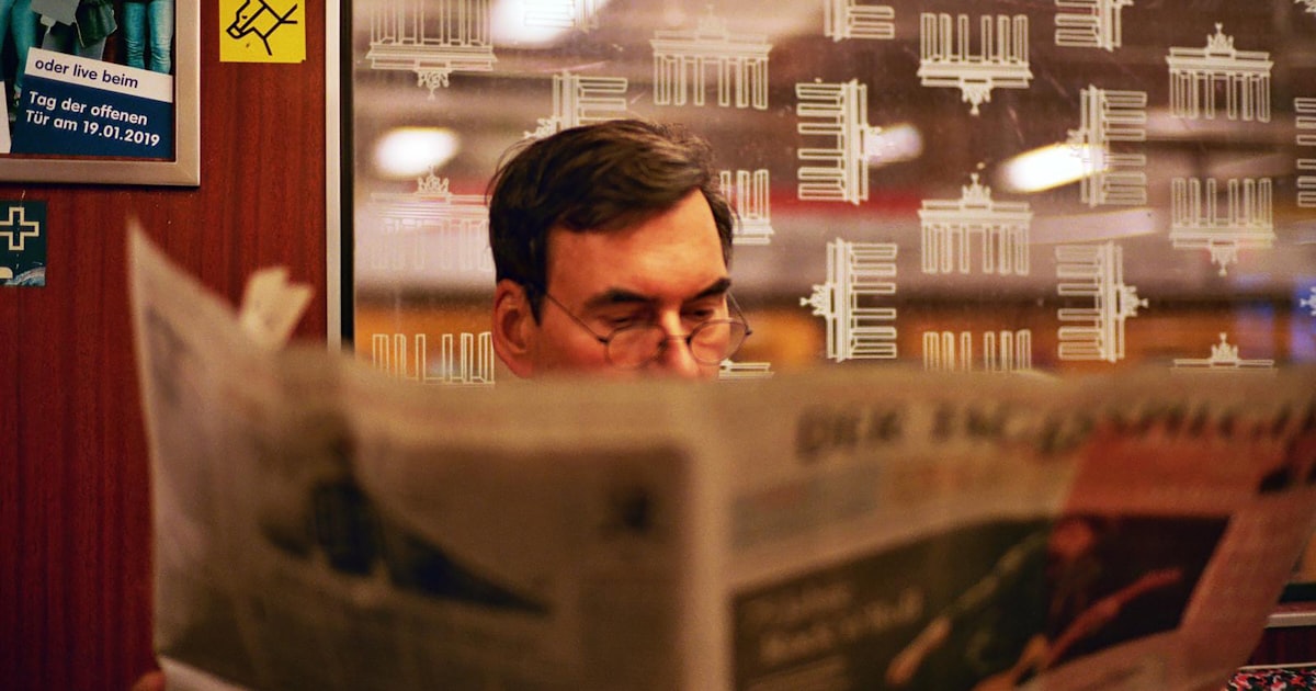 a man reading a newspaper in front of a window