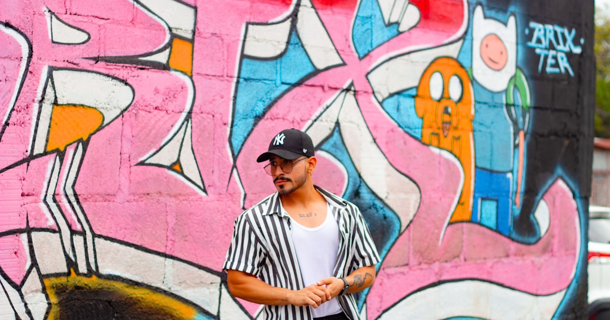Man in striped shirt stands against graffiti wall