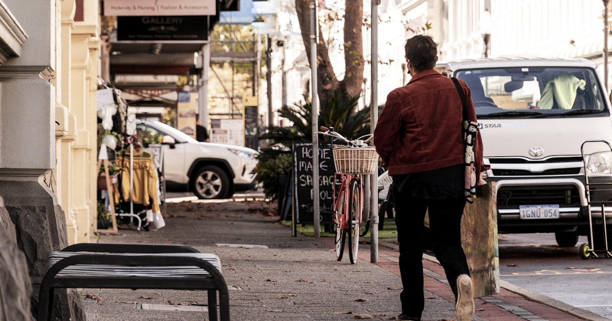 man in red shirt and black pants standing on sidewalk during daytime