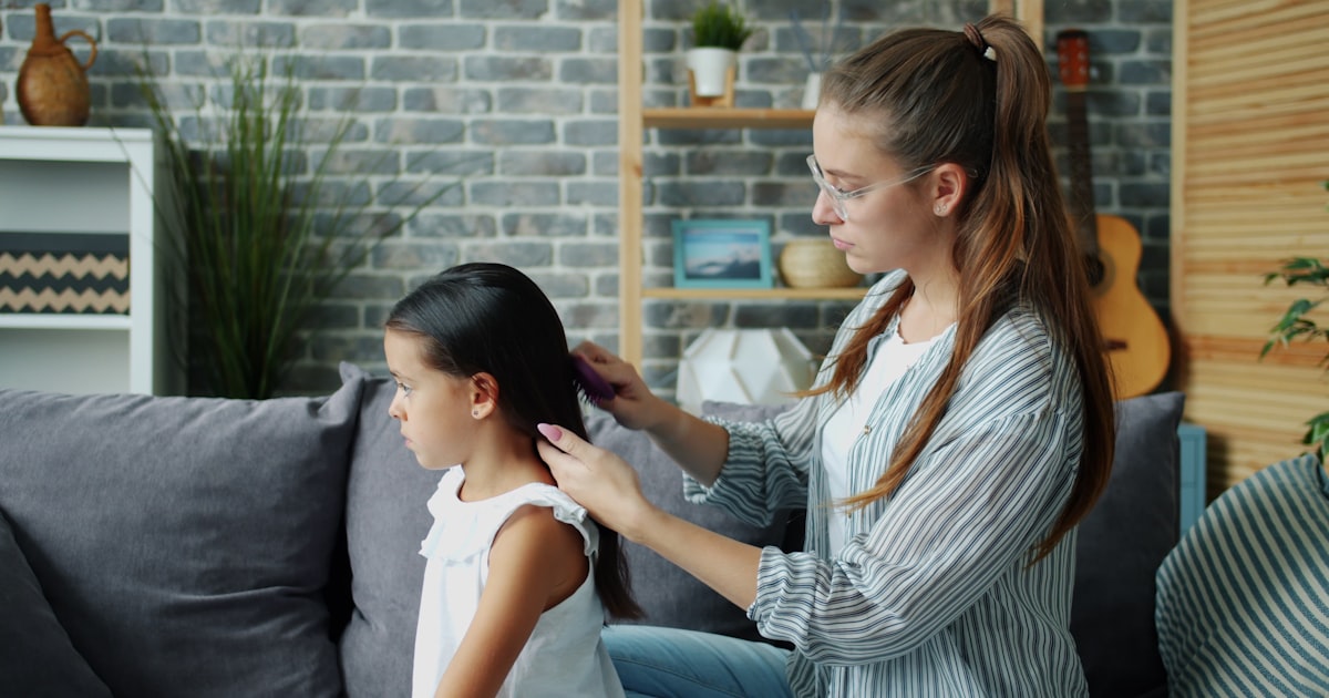 Mother combs her daughter's long dark hair.