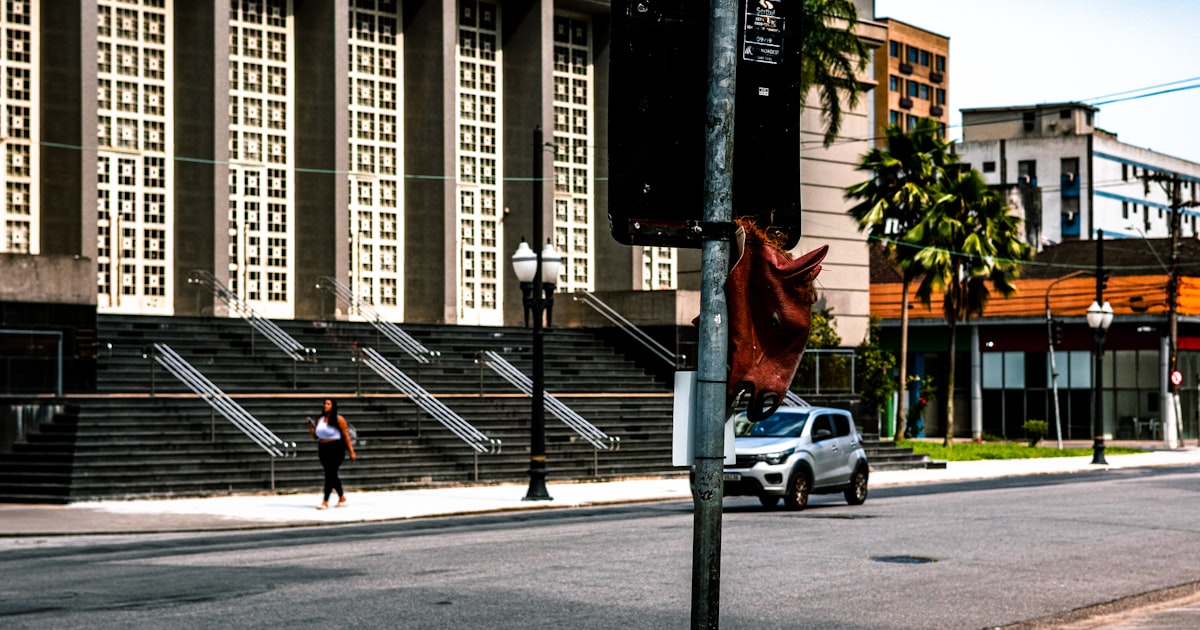 A silver suv drives past a large building with stairs.