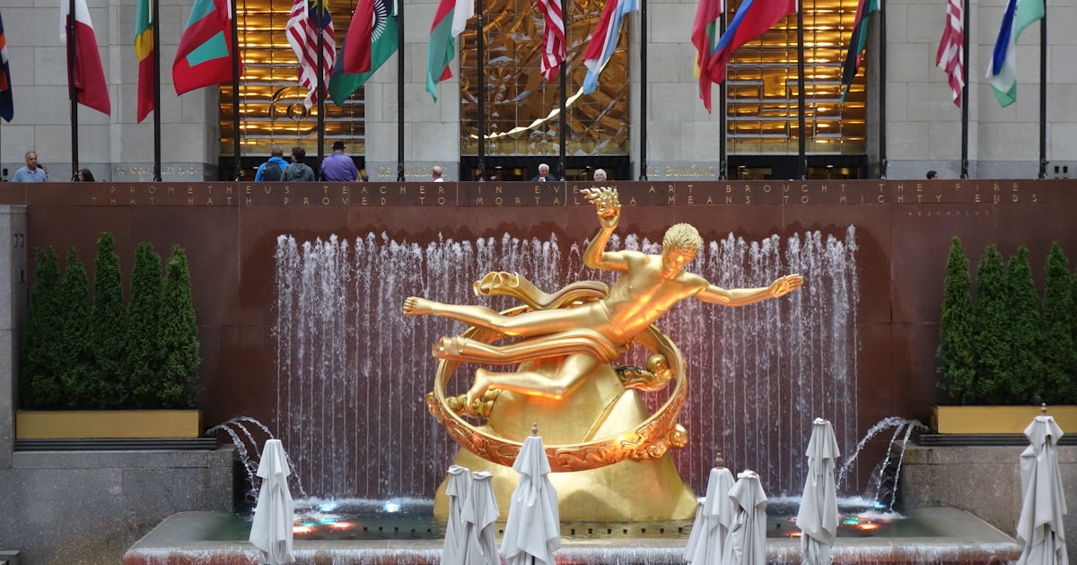 a golden statue in front of a fountain with flags in the background