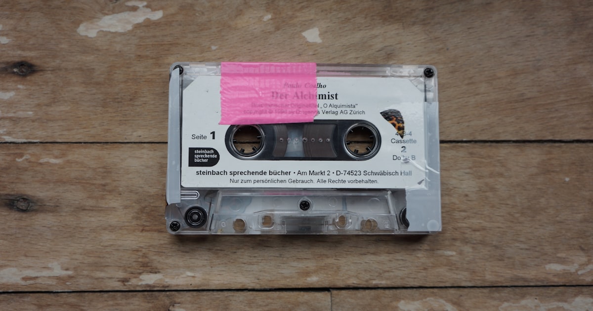 a cassette with a pink sticker on it sitting on a wooden floor