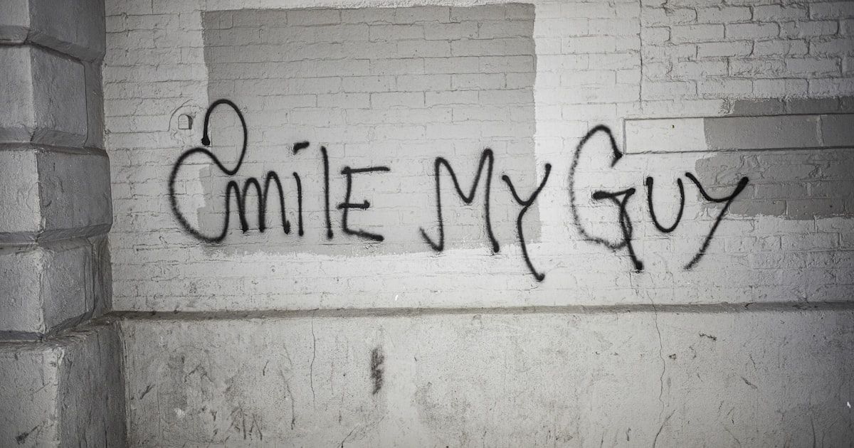 Graffiti on a brick wall says "smile my guy".