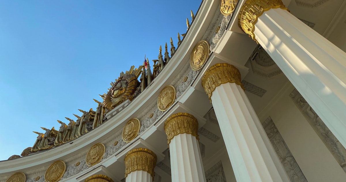 A white and gold building with columns and a sky background